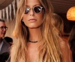 Woman with long blonde hair wearing round sunglasses and a necklace.