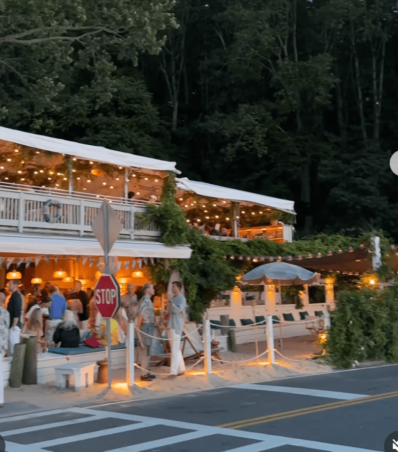 Outdoor restaurant with string lights and people dining at dusk.