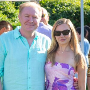 A man and woman posing outdoors on a sunny day, smiling at the camera.