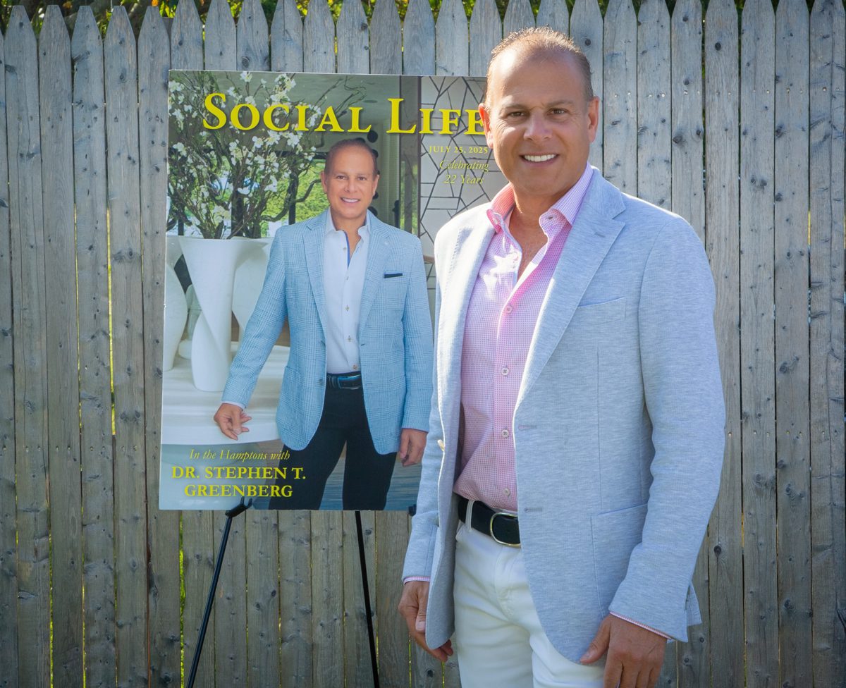 Man in light blue blazer posing next to a magazine cover featuring his photo.