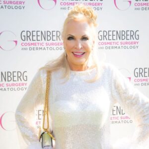 A woman in a shimmering white dress poses at a cosmetic surgery event.