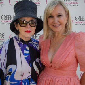 Two women posing at a cosmetic surgery event, dressed stylishly and smiling.