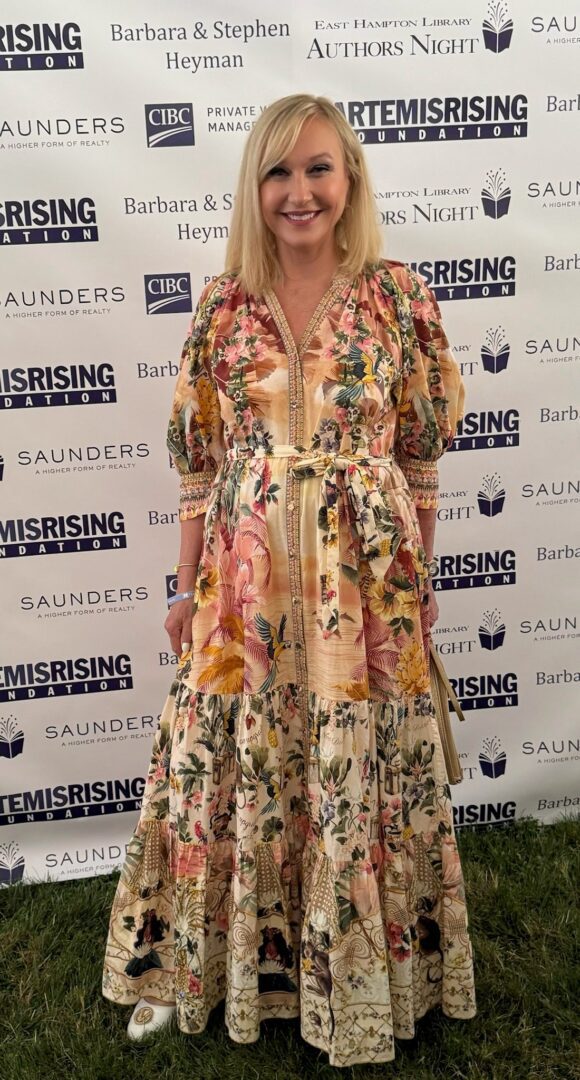 Woman in floral dress posing at a branded event backdrop.