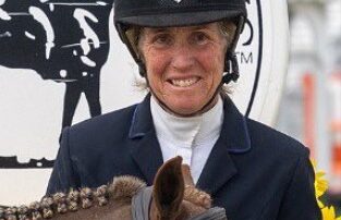 Equestrian rider smiling with horse and blue ribbon at competition.