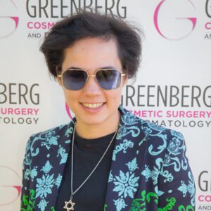 Person wearing sunglasses and a floral blazer smiling at a cosmetic surgery event.