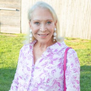 Smiling elderly woman in a floral blouse outdoors.