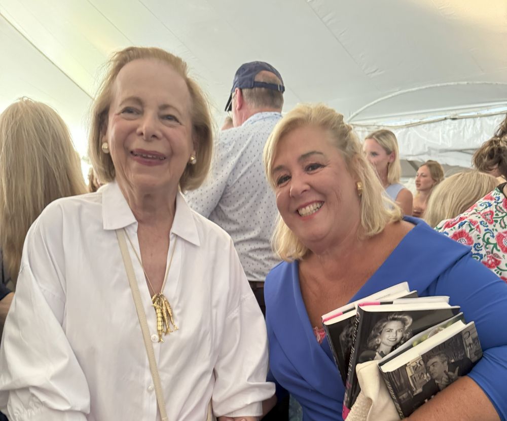 Two smiling women posing at an indoor event under a tent.