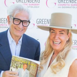 Two smiling people posing with a magazine at a cosmetic surgery event.