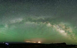 Starry night sky with Milky Way and aurora above dark landscape.