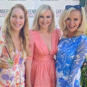 Three women smiling at an outdoor event with colorful dresses.