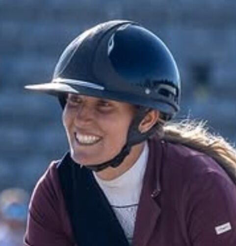 A smiling woman wearing a black equestrian helmet and maroon jacket.