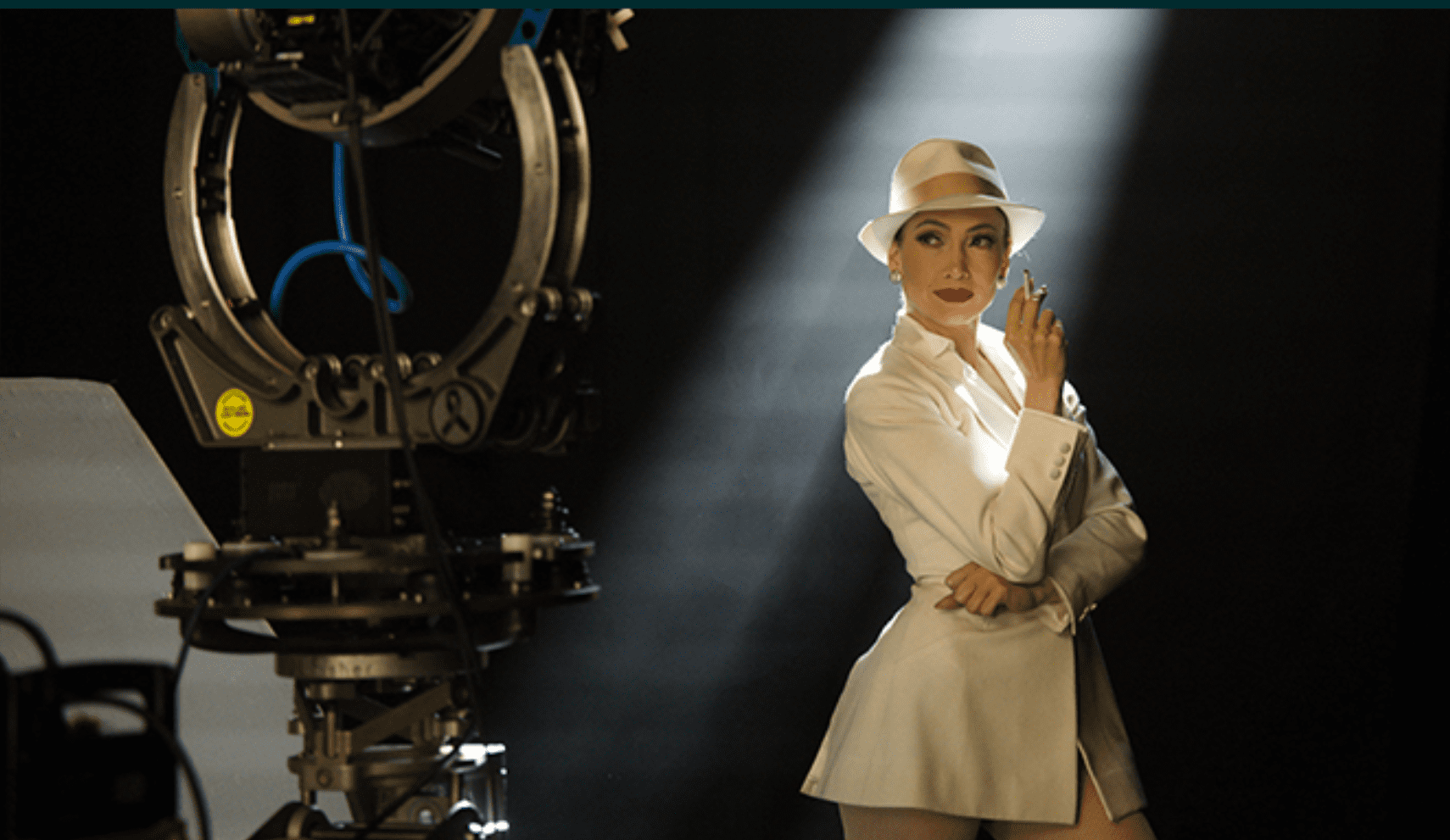 Woman in white suit and hat posing near vintage film equipment.