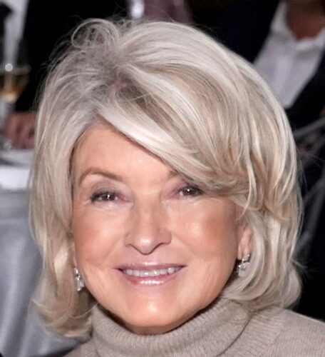 Smiling elderly woman with short blonde hair and earrings.