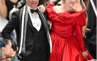 A man in a tuxedo and a woman in a red dress pose at a formal event.