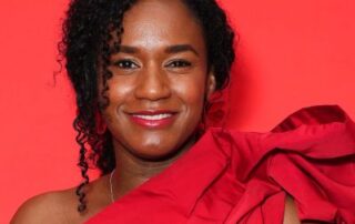 Woman smiling in a vibrant red dress against a red background.