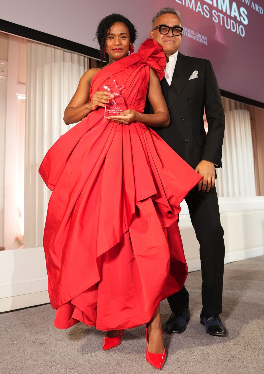 Elegant couple with a woman in a red gown holding an award and a man in a black suit.