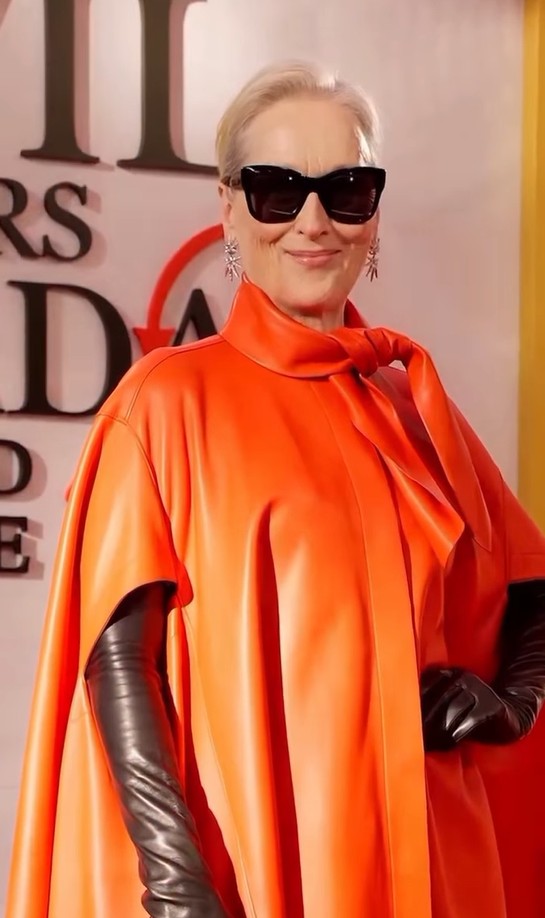 Person in bright orange satin outfit with black gloves and sunglasses.