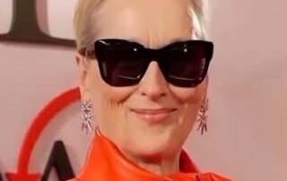 Woman wearing large black sunglasses and an orange outfit, smiling.